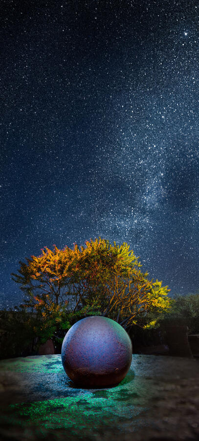 A vertical surreal light painting of a large iridescent sphere on a stone slab against a high-definition Milky Way starscape.