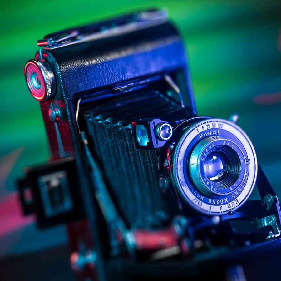 A vintage Kodak Bellows camera highlighted with vibrant cyan and magenta light painting.