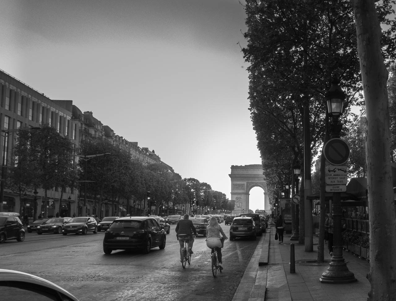 Black and white photo of a couple bicycling up the avenue des Champs-Élysées in Paris, France.